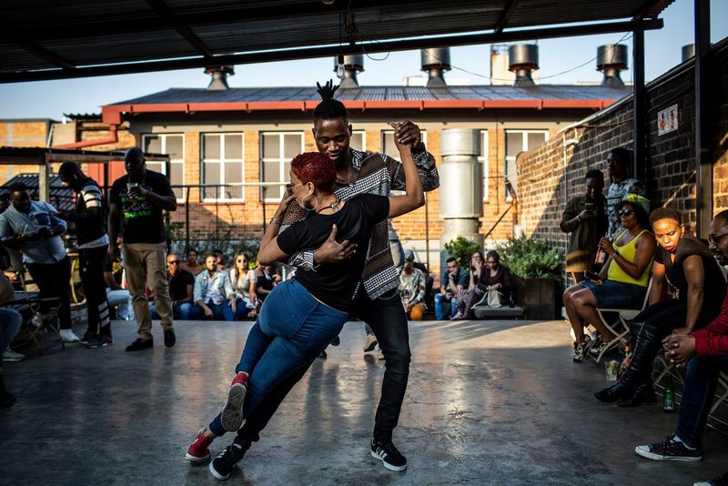 شخصان يرقصان الصلصا في حلبة رقص على سطح وتشاهدهما مجموعة من الناظرين الجالسين إلى جانبهم.