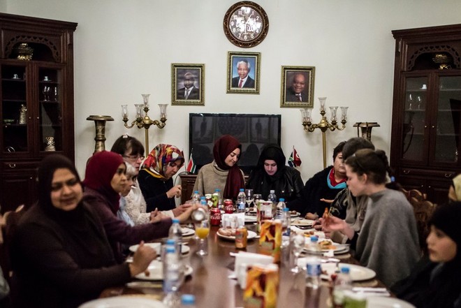 مجموعة من النساء يجلسن حول طاولة طعام طويلة مليئة بالطعام وزجاجات المشروبات الغازية.