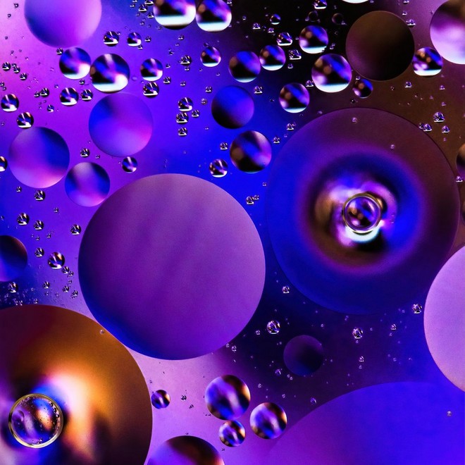 Makrofotó olajról a vízben, amely kör alakú, lila színű cseppeket hoz létre.