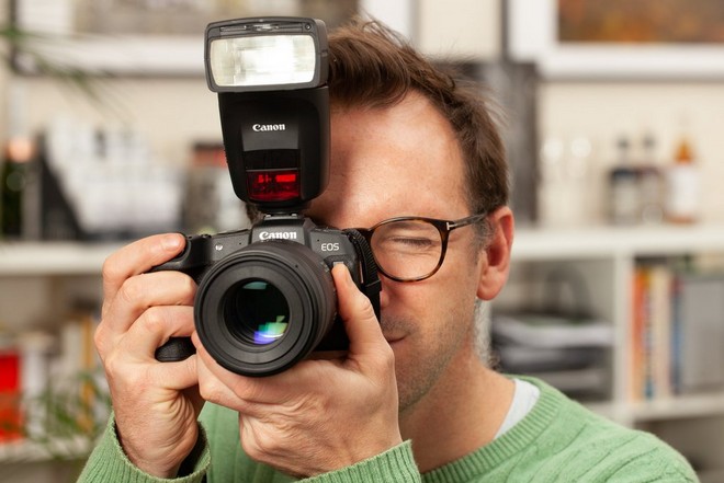رجل ينظر عبر محدد مناظر كاميرا EOS RP من Canon متصلة بفلاش Speedlite.