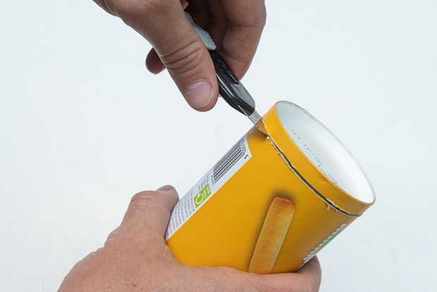 A man cutting the top off a snack food tube with a craft knife.