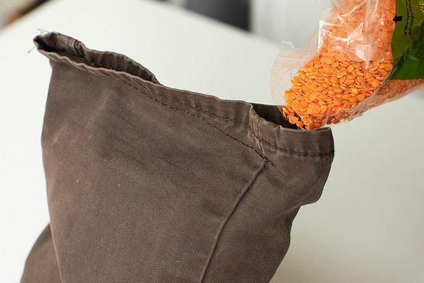 Red lentils being poured into the opening at the top of a cut-off trouser leg.