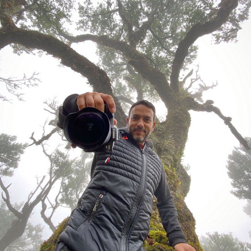 سفير Canon جويل سانتوس يقف تحت ظل شجرة كبيرة وهو يحمل كاميرا Canon.