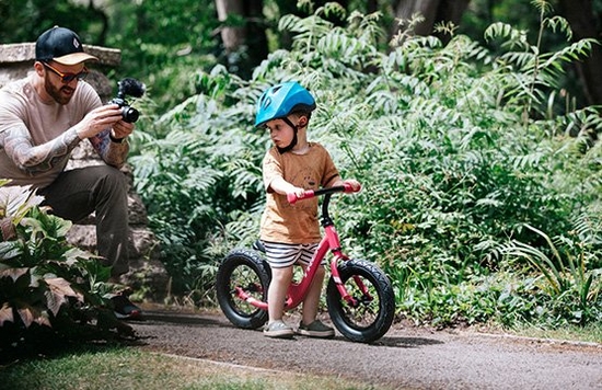 Stef Michalak crouching on a path with a Canon EOS M50 to film his son's first ride on a balance bike.