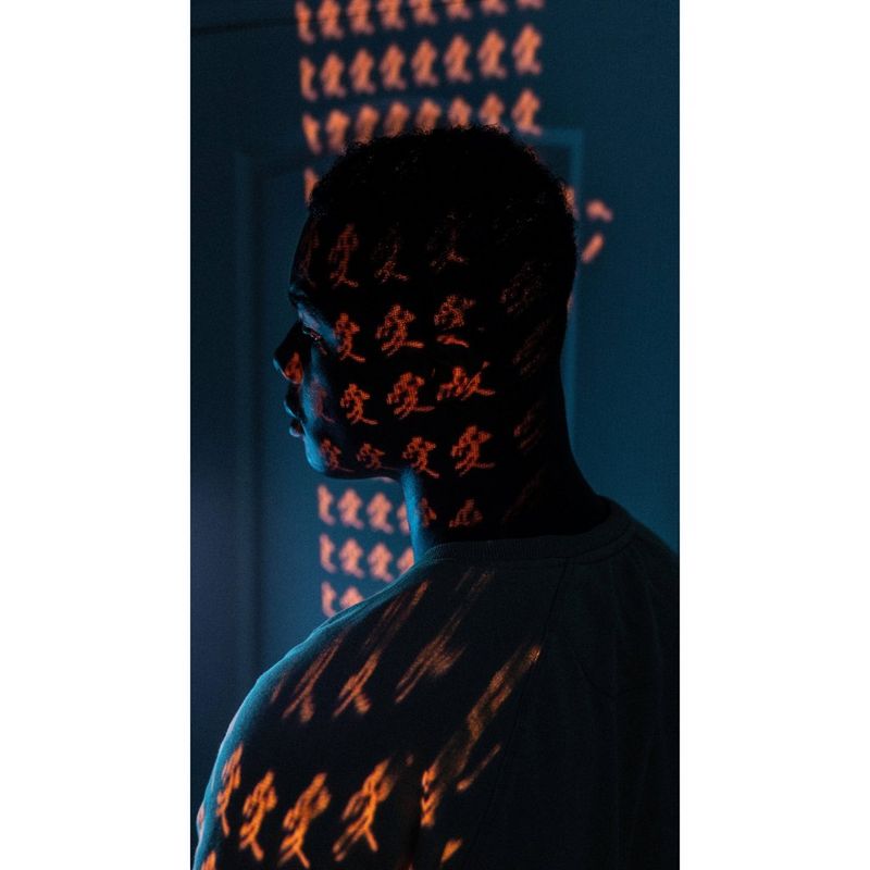 صورة شخصية لرجل مع وجود حروف صينية تنعكس على وجهه بواسطة جهاز عرض.