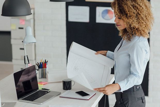 A woman stands in an office holding a sheet of paper.