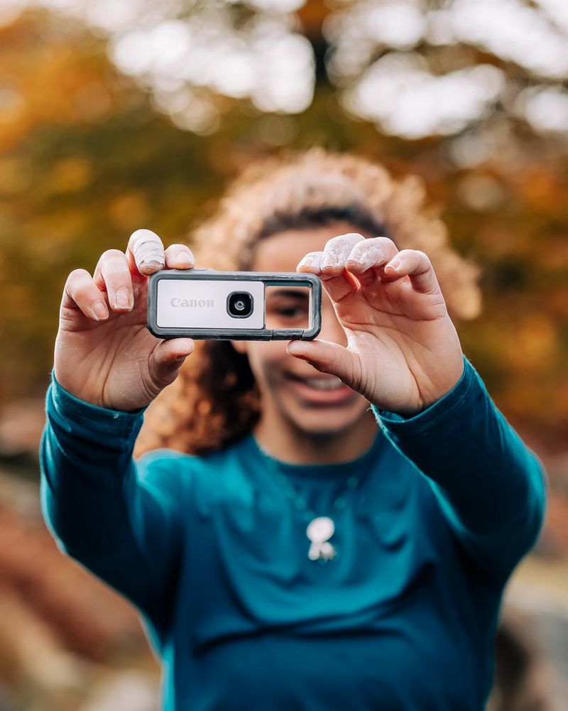 A young woman looking through the viewfinder of a Canon IVY REC activity camera.