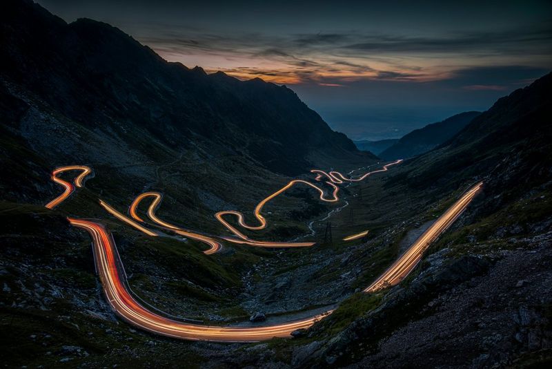Scie luminose di sera su una tortuosa strada di montagna, chiaramente visibili in lontananza. Scatto realizzato da Piotr Skrzypiec con Canon EOS R5.