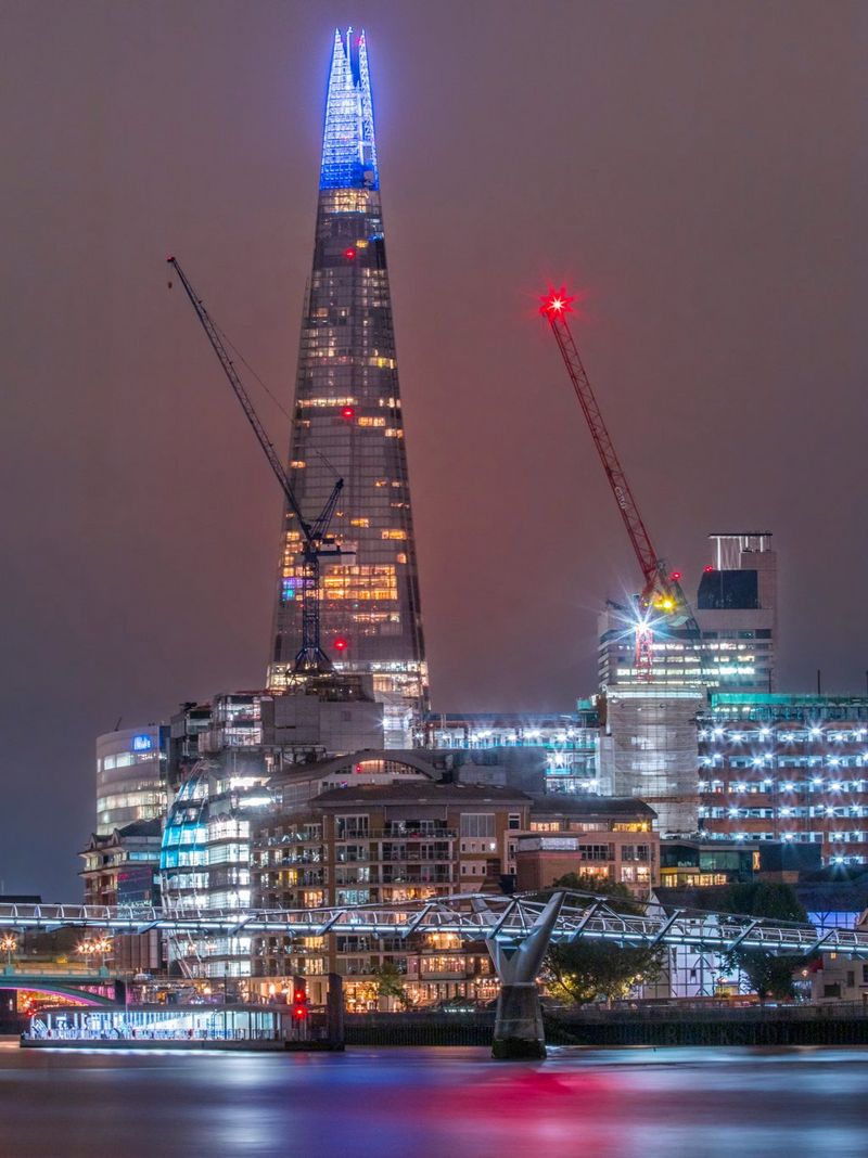 A night-time shot of The Shard in London towering over Southwark, the buildings lit up in lights. The London Millennium Footbridge can be seen in the foreground.