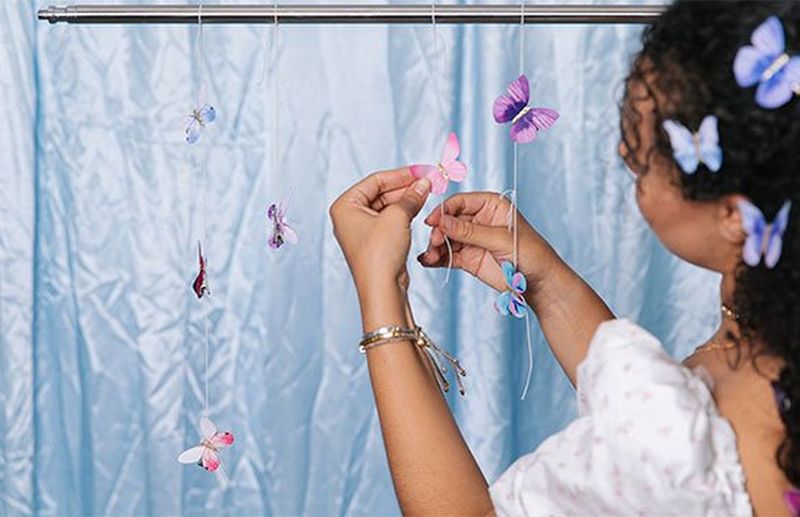 A woman with butterfly clips in her hair fastens more butterfly clips to pieces of string hanging from a silver bar.