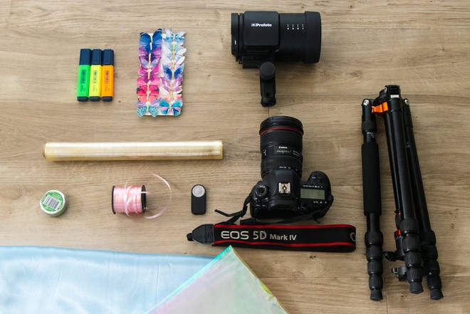 كاميرا EOS 5D Mark IV من Canon وحامل ثلاثي القوائم وأدوات مكتبية متنوعة موضوعة على سطح الطاولة.