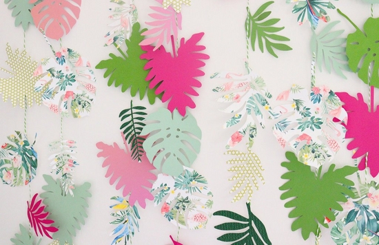A wall hanging made of tropical leaf shapes, cut out of colourful paper in pinks and greens and tropical prints.