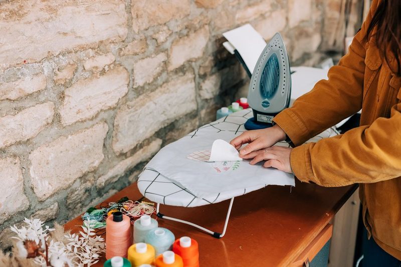A woman peeling backing paper off a transfer attached to a white sheet of fabric.
