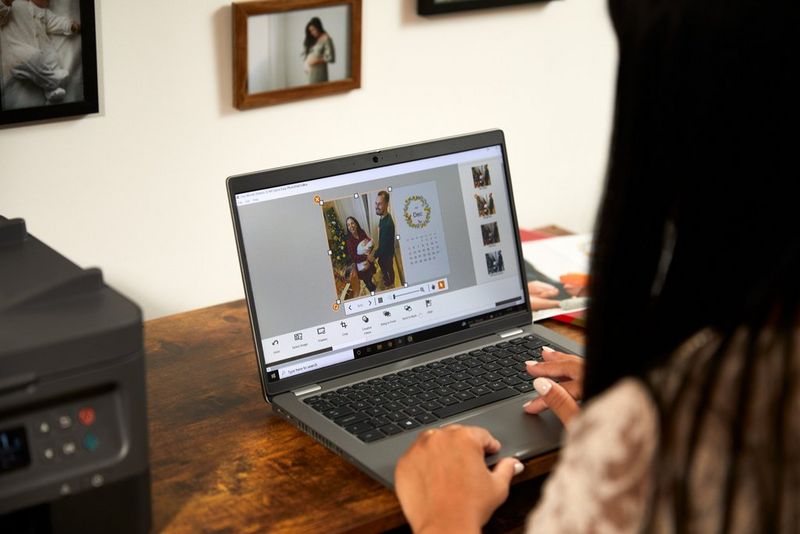 Жена седи со лаптоп, прилагодува семејни фотографии во календар со фотографии со помош на Easy-PhotoPrint Editor од Canon.