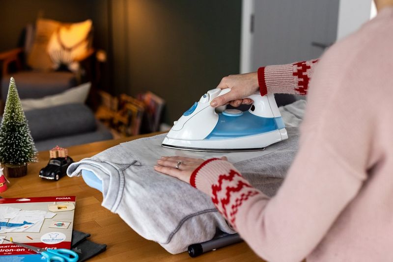 Жена пегла хартија за пренос на слики врз сив џемпер.