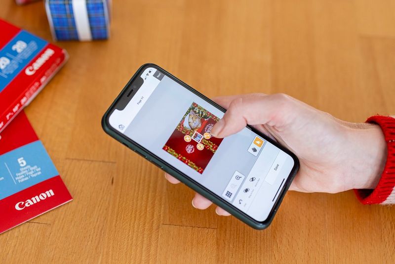 Некој користи паметен телефон за да го уреди дизајнот на својата божиќна честитка со помош на апликацијата Easy-PhotoPrint Editor.