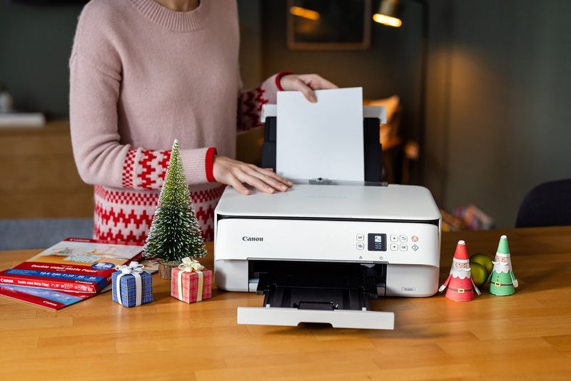 Жена во божиќен џемпер става хартија во печатач PIXMA од Canon.