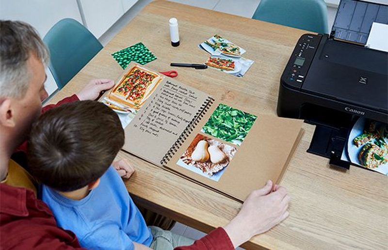 A father and son flick through the pages of a recipe book together. 