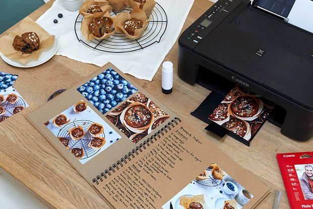 A top-down shot of a printer, a recipe book and muffins on a cooling rack. 