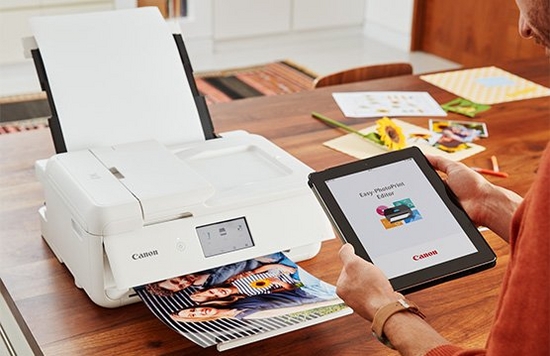 A tablet displays the Canon Easy-PhotoPrint App while a printer prints a picture. 