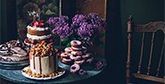 A low-light shot, featuring a table of cakes and flowers. 