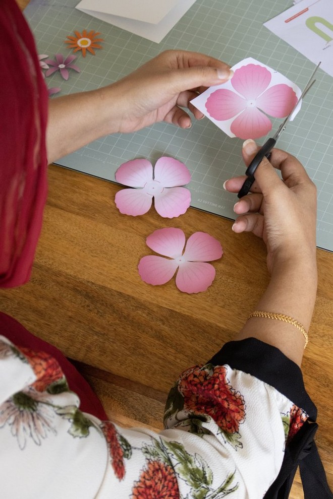 Женски раце сечат розови цветови од хартија со ножици.