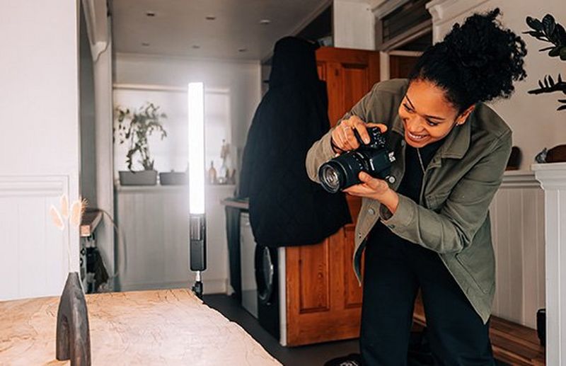 A woman using a EOS 850D to photograph a wooden vase on a table, lit by an LED light.