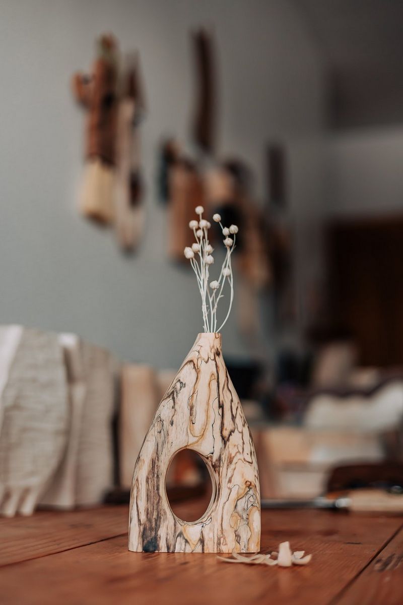 A wooden vase filled with some small white flowers on a table against a blurred background.