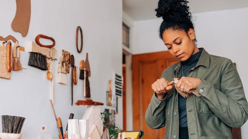 A woman hand carving a wooden vase in her workshop.