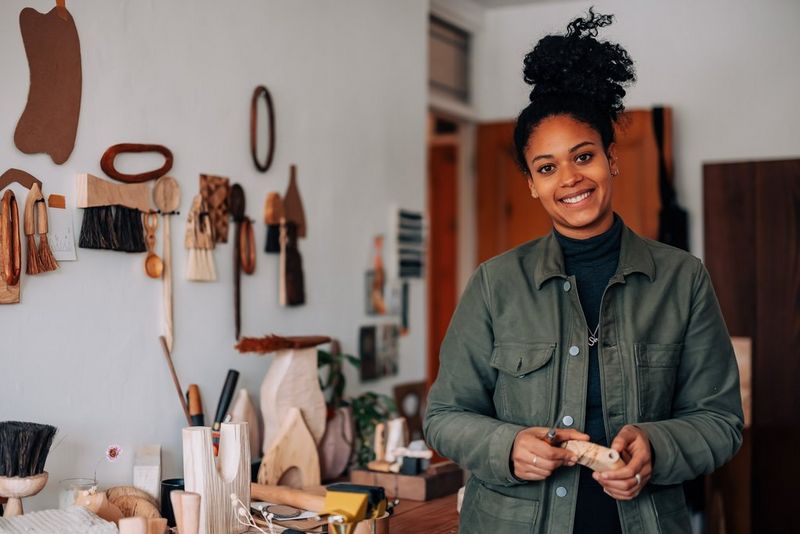 A woman standing in her workshop, holding a wooden vase.