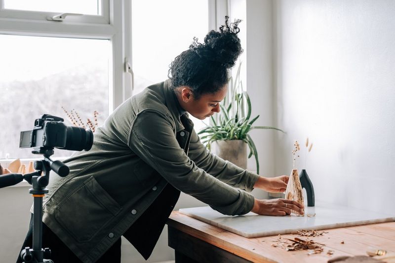 A woman arranging a hand carved vase to shoot with her EOS 850D on a tripod.