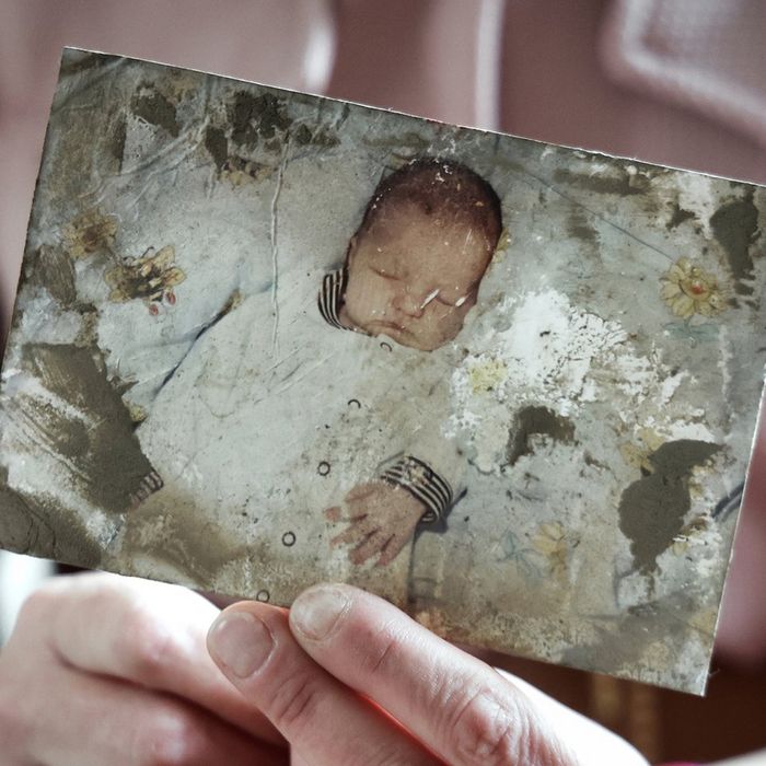 Hands holding a damaged photograph of a sleeping baby.