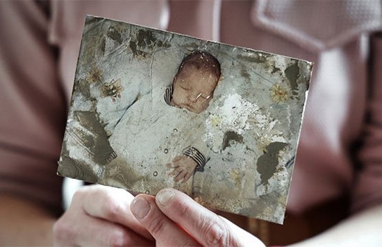 Hands holding a damaged photograph of a sleeping baby.