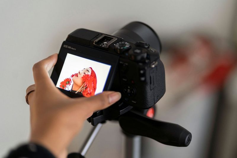 A hand adjusting the flip-up touchscreen on a Canon EOS M6 Mark II fixed to a tripod.