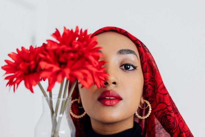 Photographer and poet Amaal Said wearing a red patterned headscarf. A vase of red flowers is partly obscuring her face.