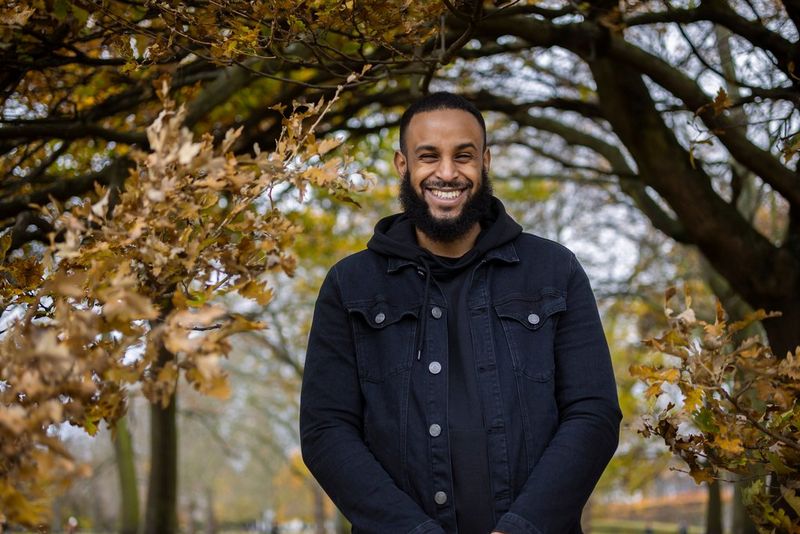 A portrait of a man standing in a park framed by autumn leaves.