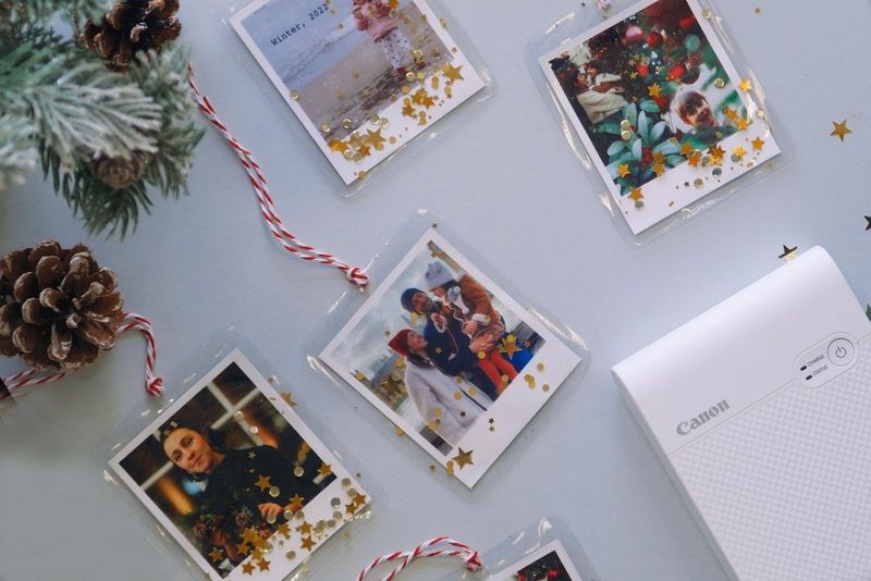 Ülalt alla tehtud pilt, millel on fotodega jõulukaunistuste valik Canon SELPHY Square QX10 printeri kõrval.