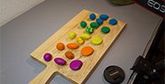 A wooden chopping board with balls of colourful clay spread along it. 