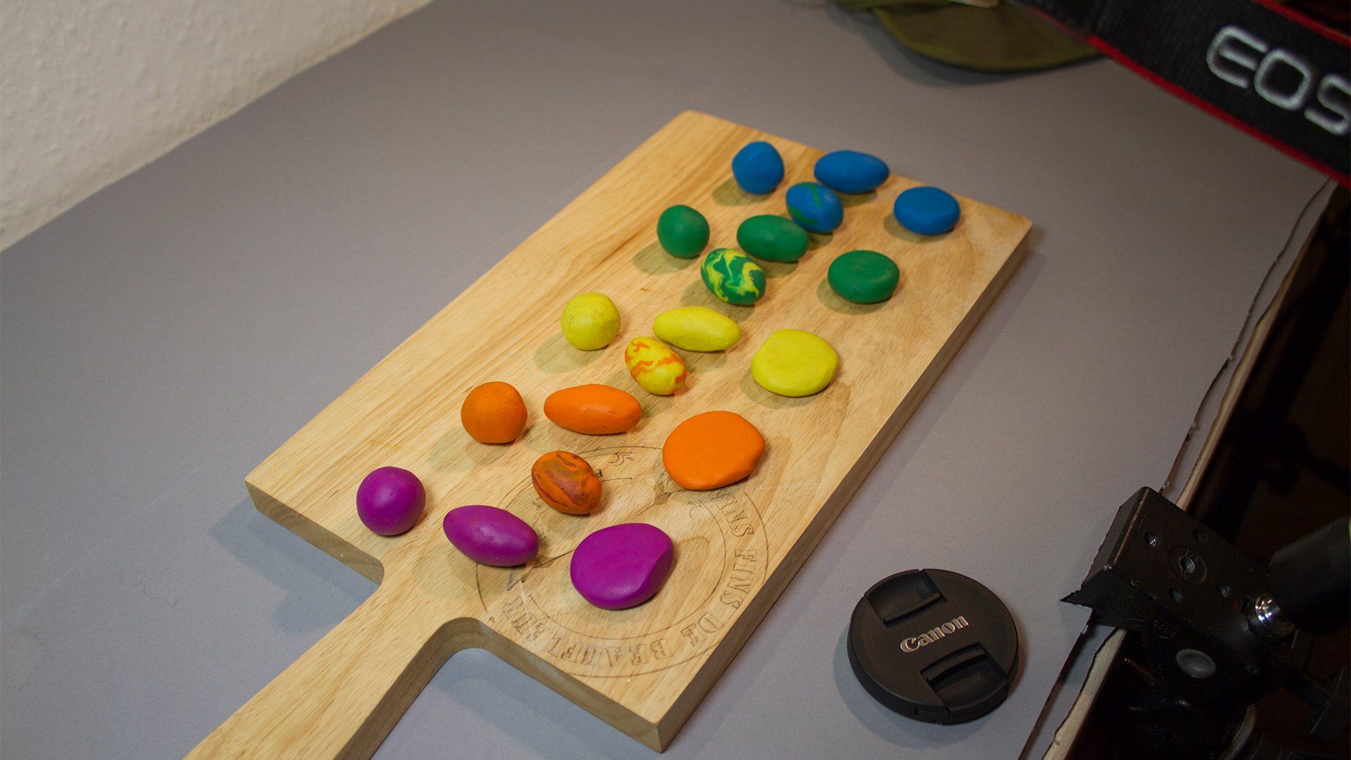 A wooden chopping board with balls of colourful clay spread along it.