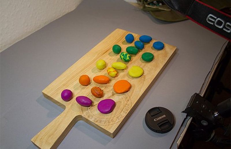 A wooden chopping board with balls of colourful clay spread along it.