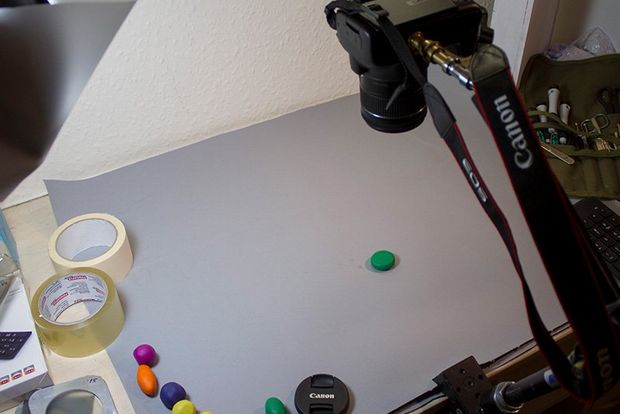 Uma câmera EOS em um tripé apontando para uma pequena bola de barro verde em uma mesa