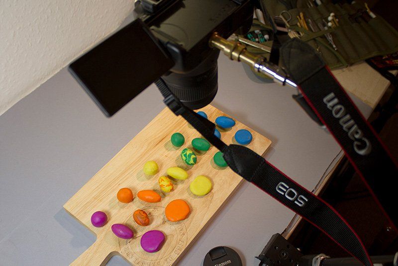 A Canon EOS camera on a tripod, pointing down at a chopping board covered with balls of brightly coloured clay.
