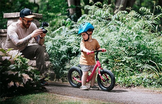 Stef Michalak crouching on a path with a Canon EOS M50 to film his son's first ride on a balance bike.