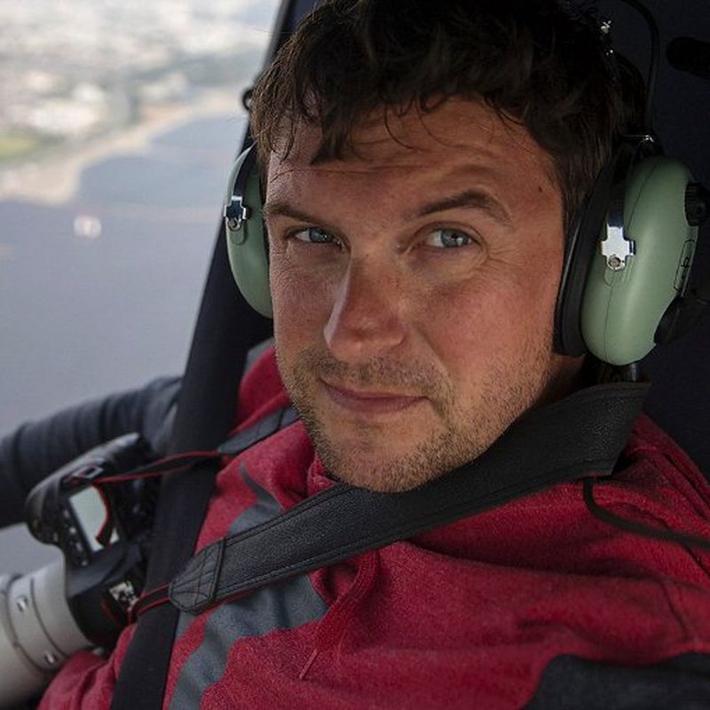Headshot of a person dressed in red wearing headphones at the window of a small aircraft.