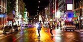 Two people skateboarding down a bustling street at night.