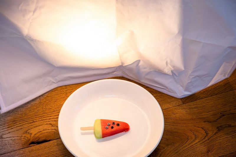 A desk lamp shines through a piece of fine gauze fabric, illuminating an ice cream on a plate.