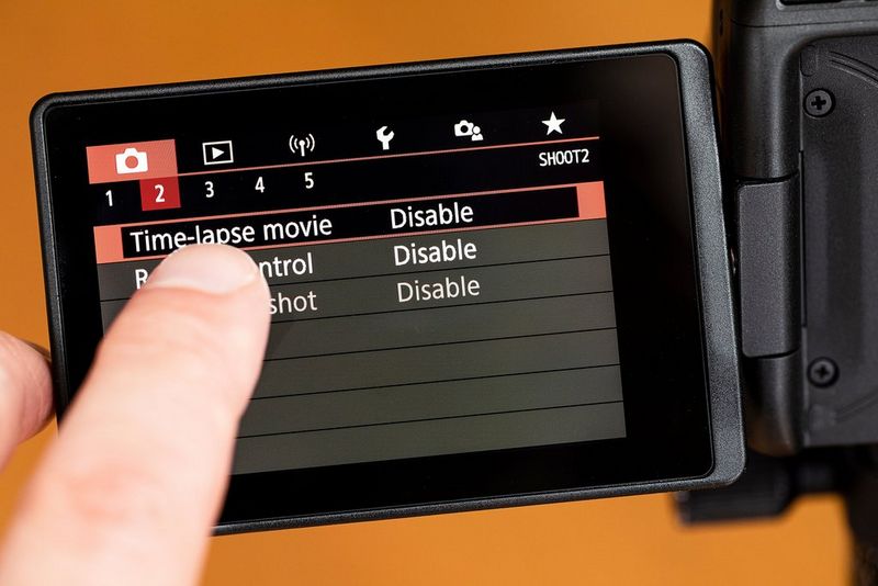 A user's finger selecting Time-lapse movie mode on a Canon camera's vari-angle touchscreen.