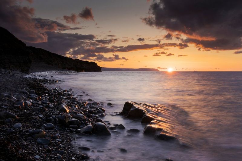Λήψη της θάλασσας με μακρά έκθεση και θόλωμα μπροστά από τους βράχους μιας ακτής στο ηλιοβασίλεμα.