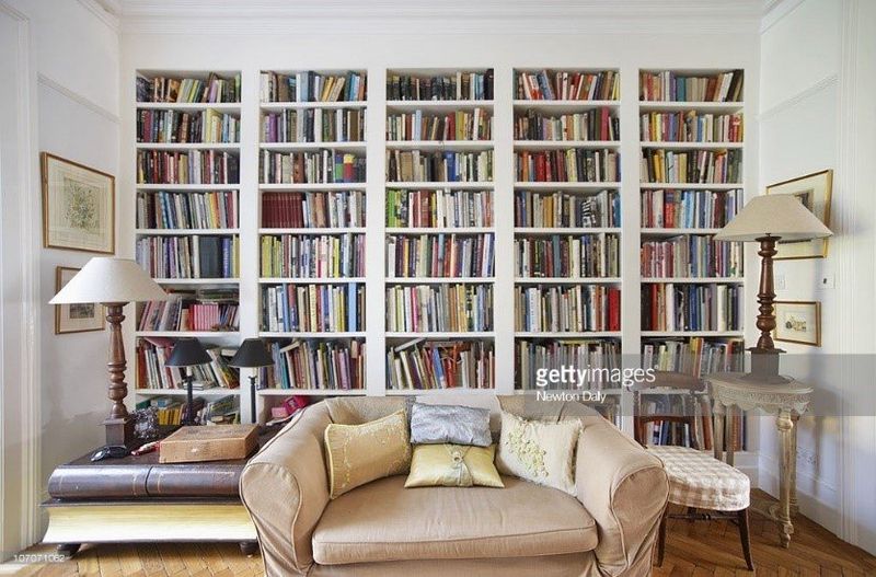 Image of a living room with a colourful bookcase across the back wall, two large table lamps on side tables and a two-seater silk sofa in the middle.