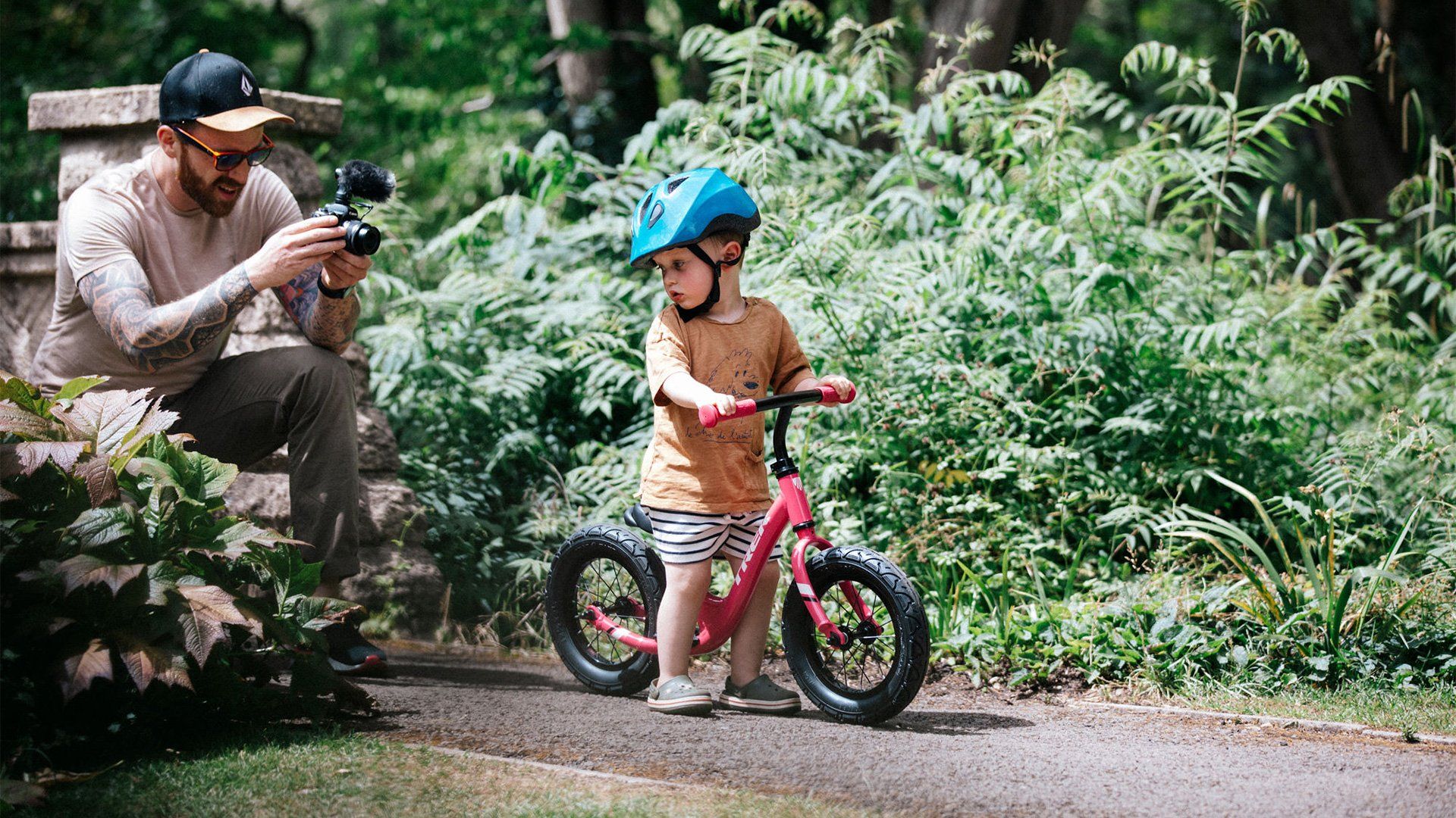 Stef Michalak crouching on a path with a Canon EOS M50 to film his son's first ride on a balance bike. 